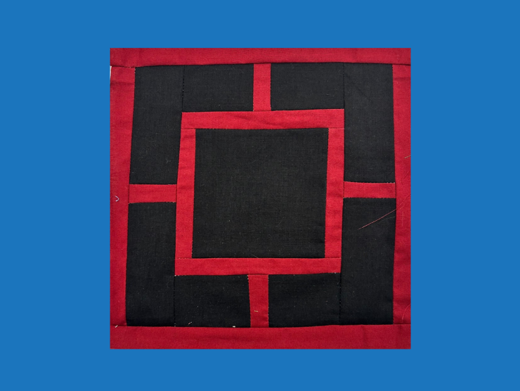 A blue background with a red and black square quilt block on top. The quilt block has a black square in center and black L shaped blocks on each corner. There are red lines defining each block/square.