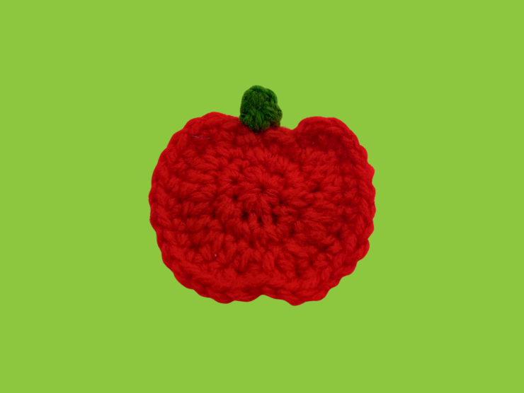 A green background with a crocheted red apple and green leaf