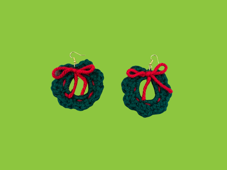 A bright green background that has two green wreaths with red bows attached to earring hooks in the center.